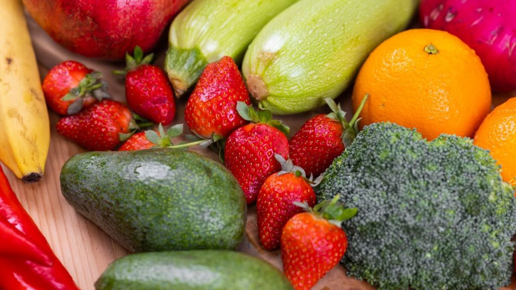 A vibrant selection of fresh fruits and vegetables including strawberries, avocado, and broccoli on a wooden table.